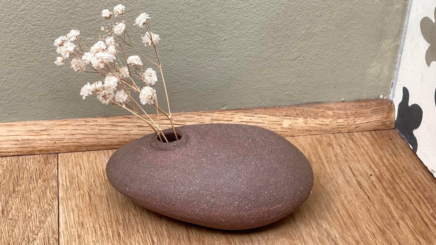 Vase-galet en grès brun avec gypsophile, posé sur une planche de bois